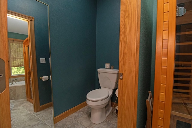 full bath featuring toilet, tile patterned floors, baseboards, and a garden tub