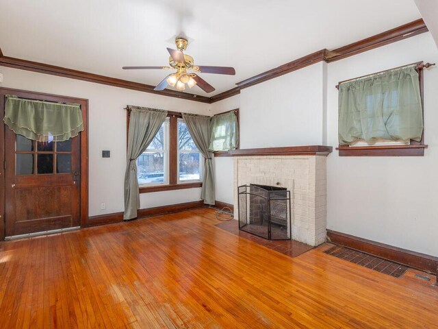 unfurnished living room with hardwood / wood-style floors, ceiling fan, crown molding, and a brick fireplace