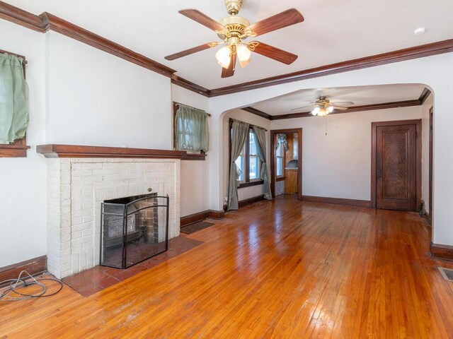 unfurnished living room with hardwood / wood-style flooring, ceiling fan, ornamental molding, and a brick fireplace