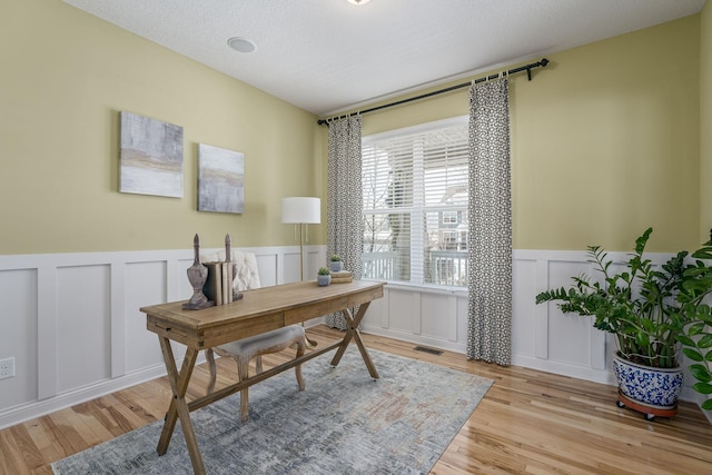 office area featuring a textured ceiling, a decorative wall, a wainscoted wall, wood finished floors, and visible vents