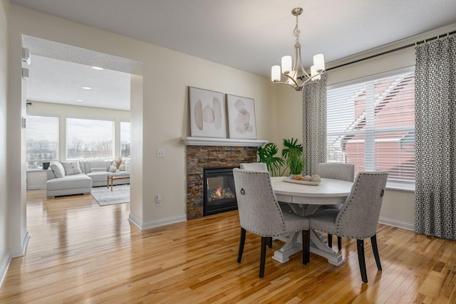 dining area with light wood finished floors, a fireplace, baseboards, and a notable chandelier