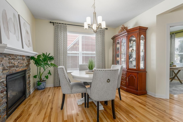 dining space featuring baseboards, a stone fireplace, light wood-type flooring, and a notable chandelier