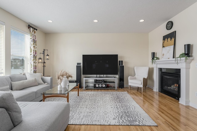 living area featuring baseboards, a glass covered fireplace, wood finished floors, a textured ceiling, and recessed lighting