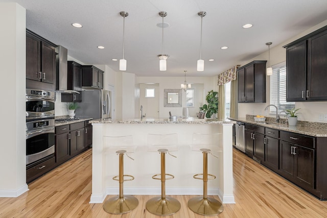 kitchen with appliances with stainless steel finishes, a center island, a sink, and light wood finished floors