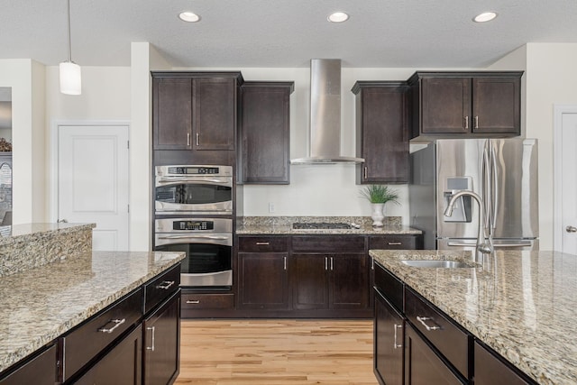 kitchen with appliances with stainless steel finishes, light stone counters, light wood-style flooring, and wall chimney exhaust hood