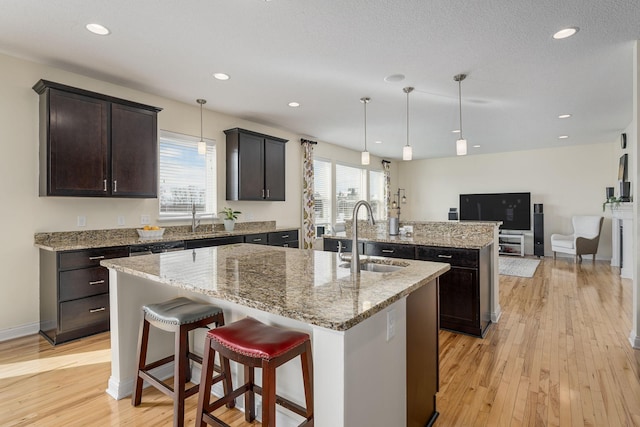 kitchen with a sink, open floor plan, light wood-type flooring, an island with sink, and decorative light fixtures