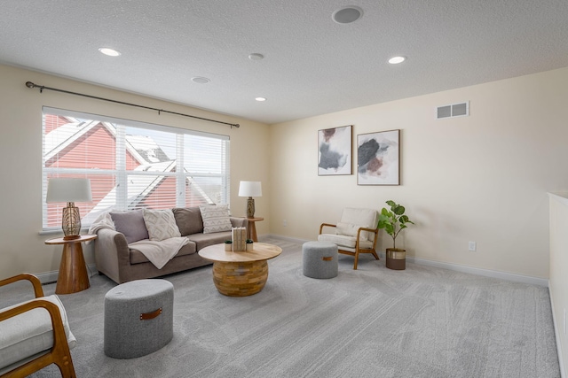 living area with a textured ceiling, carpet, visible vents, and baseboards