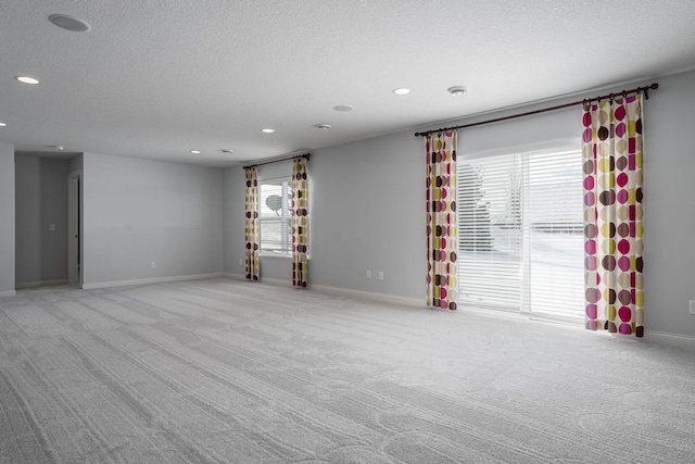 empty room with recessed lighting, light carpet, a textured ceiling, and baseboards