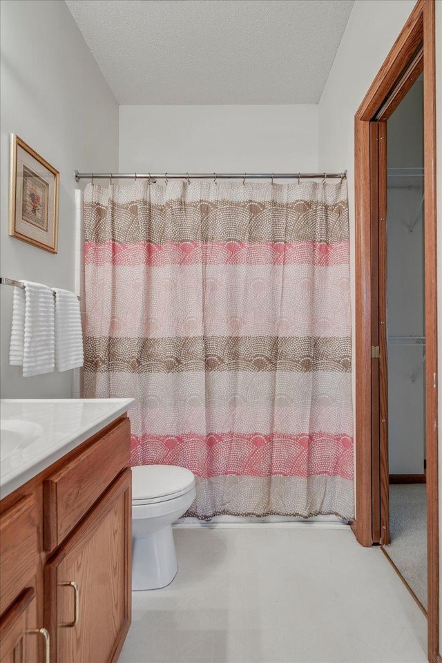 bathroom with vanity, a textured ceiling, walk in shower, and toilet