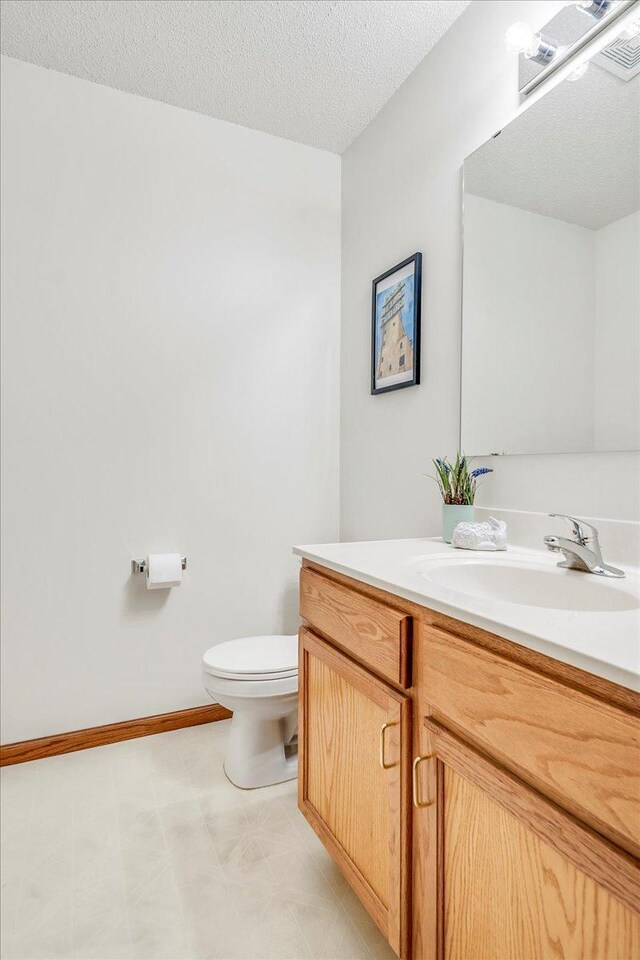 1229 Clarence St, Saint Paul, MN 55106 - half bath featuring vanity, toilet, a textured ceiling, and baseboards