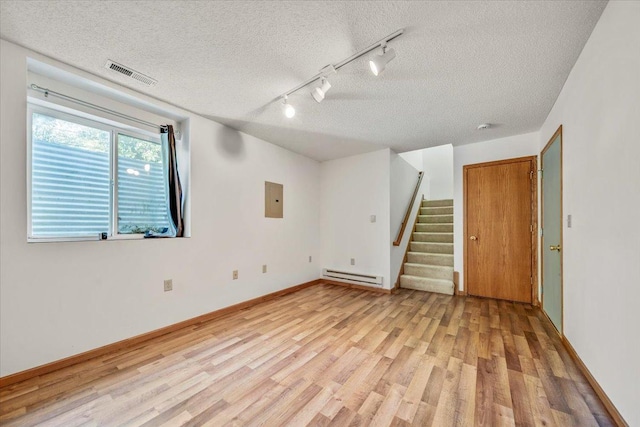 empty room with track lighting, light hardwood / wood-style flooring, a baseboard heating unit, electric panel, and a textured ceiling