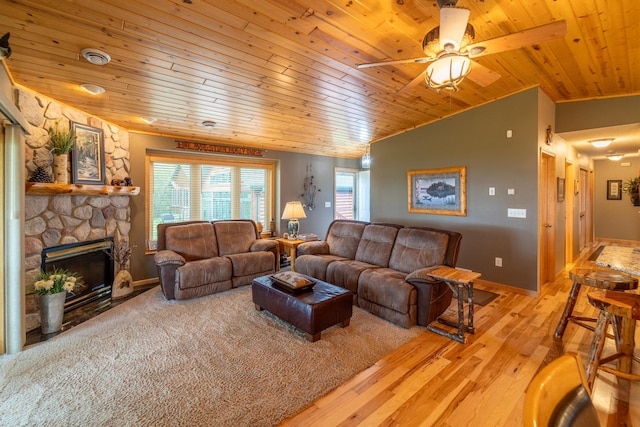 living room featuring lofted ceiling, wooden ceiling, a stone fireplace, and light hardwood / wood-style flooring