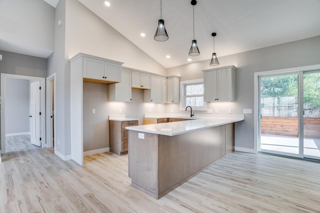 kitchen with high vaulted ceiling, kitchen peninsula, pendant lighting, light wood-type flooring, and sink