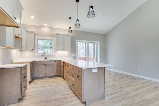 kitchen with lofted ceiling, sink, a kitchen island, decorative light fixtures, and light hardwood / wood-style flooring