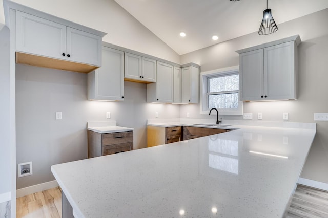 kitchen featuring pendant lighting, sink, light hardwood / wood-style flooring, light stone countertops, and vaulted ceiling