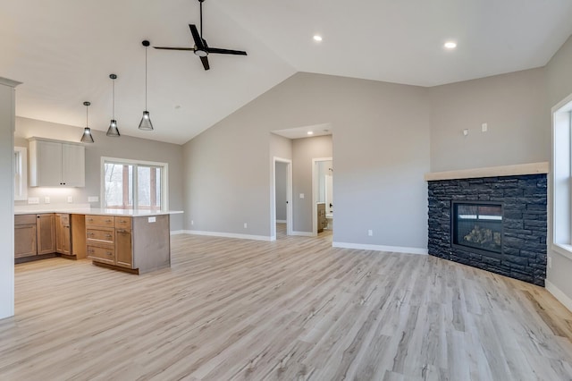 kitchen featuring hanging light fixtures, light hardwood / wood-style floors, high vaulted ceiling, a stone fireplace, and ceiling fan