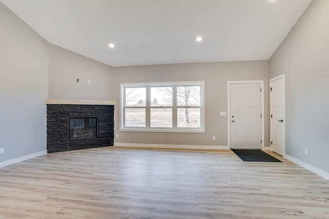 unfurnished living room featuring a stone fireplace, lofted ceiling, and light hardwood / wood-style flooring