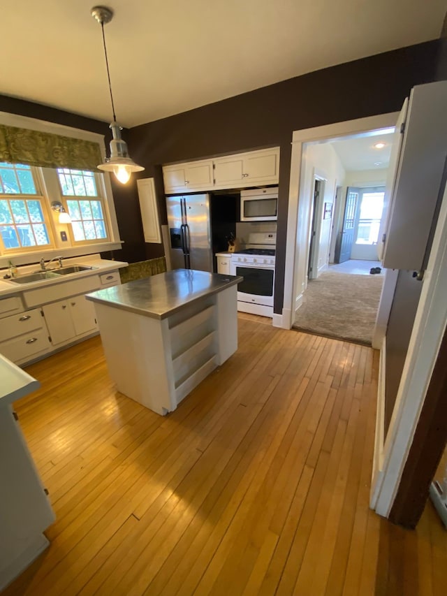 kitchen featuring sink, white appliances, light hardwood / wood-style floors, white cabinetry, and hanging light fixtures