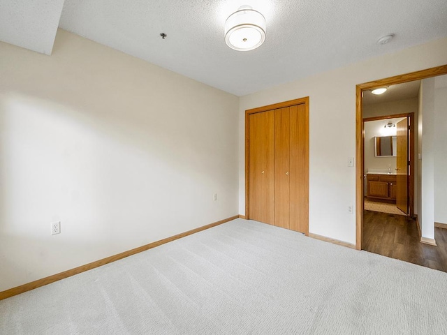 unfurnished bedroom with ensuite bathroom, a closet, and dark colored carpet