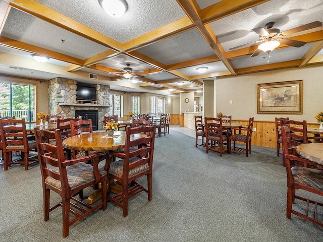 dining space featuring carpet, coffered ceiling, a textured ceiling, beam ceiling, and a stone fireplace