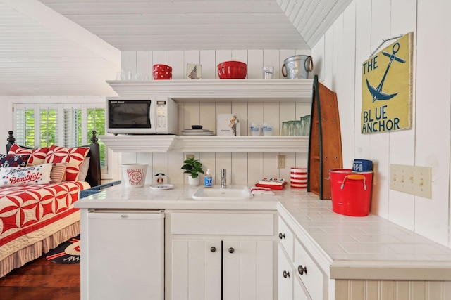 kitchen with white appliances, white cabinetry, tile counters, and sink