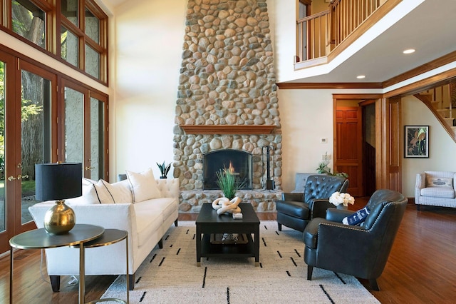 living room featuring hardwood / wood-style floors, a wealth of natural light, a stone fireplace, and a high ceiling