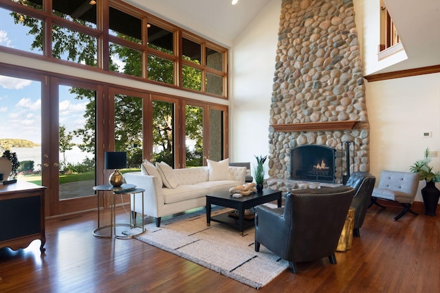 living room featuring hardwood / wood-style floors, a towering ceiling, and a stone fireplace