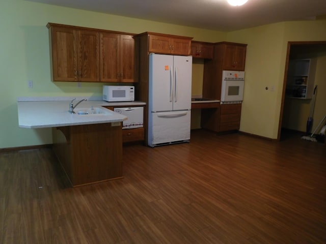 kitchen with dark hardwood / wood-style floors, white appliances, kitchen peninsula, and a breakfast bar area