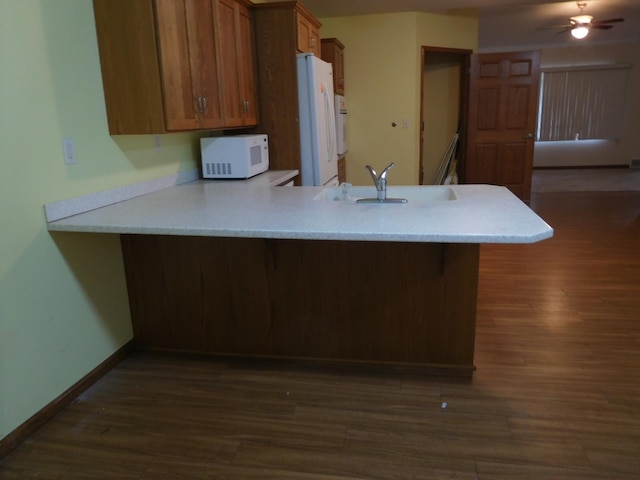 kitchen with kitchen peninsula, white appliances, dark wood-type flooring, and sink