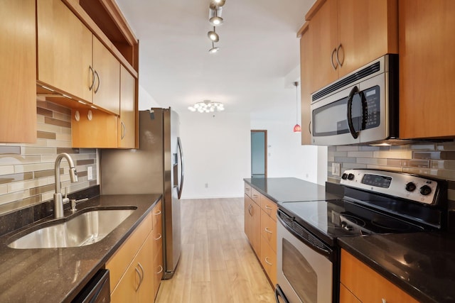 kitchen with backsplash, appliances with stainless steel finishes, light hardwood / wood-style floors, sink, and dark stone countertops