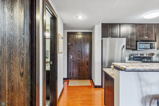 kitchen featuring stainless steel appliances, dark brown cabinets, light stone counters, and light wood-style floors