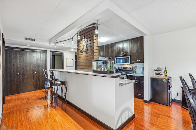 kitchen with visible vents, light wood-style flooring, appliances with stainless steel finishes, dark brown cabinets, and a kitchen bar