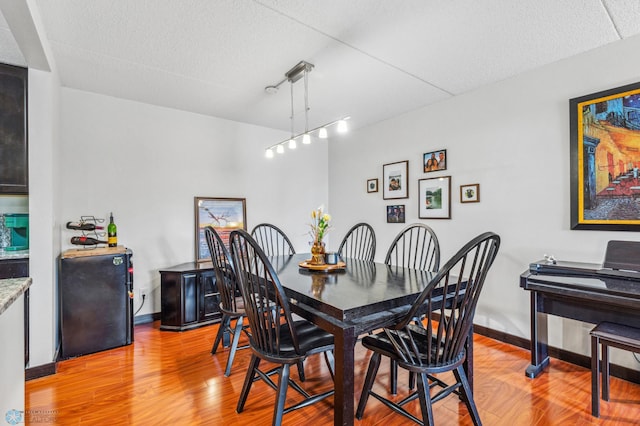 dining area featuring light wood-style floors, track lighting, baseboards, and a textured ceiling