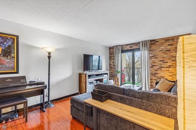 living area featuring brick wall, a textured ceiling, baseboards, and wood finished floors