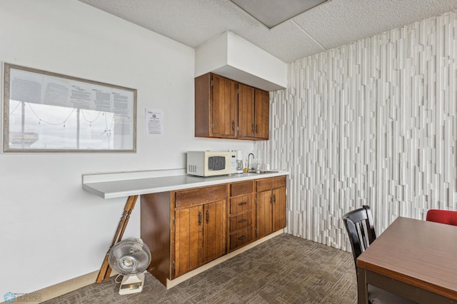 kitchen featuring white microwave, brown cabinetry, a sink, and light countertops