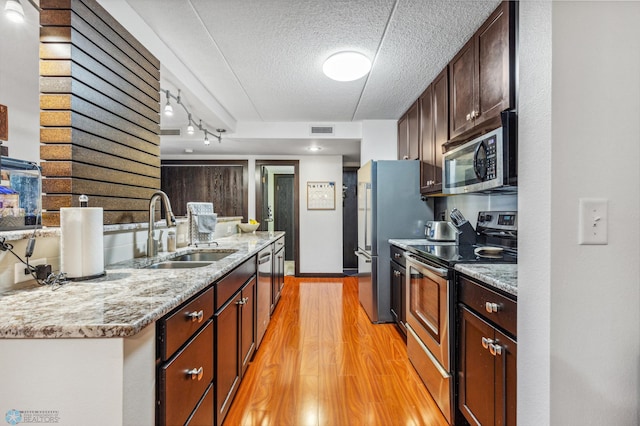 kitchen with a textured ceiling, stainless steel appliances, a sink, visible vents, and light wood-style floors