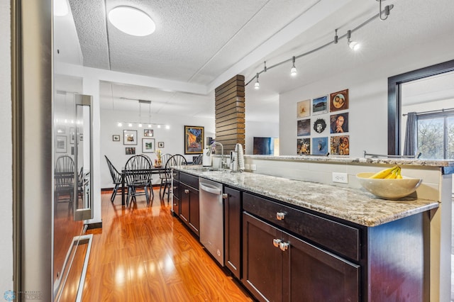 kitchen featuring stainless steel dishwasher, a sink, a textured ceiling, light stone countertops, and light wood-type flooring