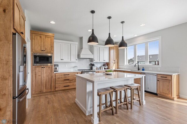 kitchen with a kitchen island, custom range hood, appliances with stainless steel finishes, and light hardwood / wood-style floors