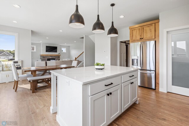 kitchen featuring a fireplace, a center island, light stone countertops, stainless steel fridge with ice dispenser, and white cabinets