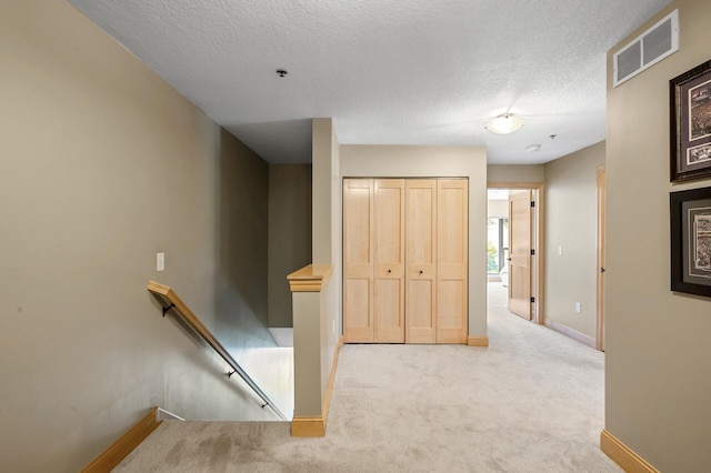 hallway with light carpet and a textured ceiling