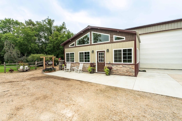 back of property featuring stone siding, board and batten siding, a patio, and fence