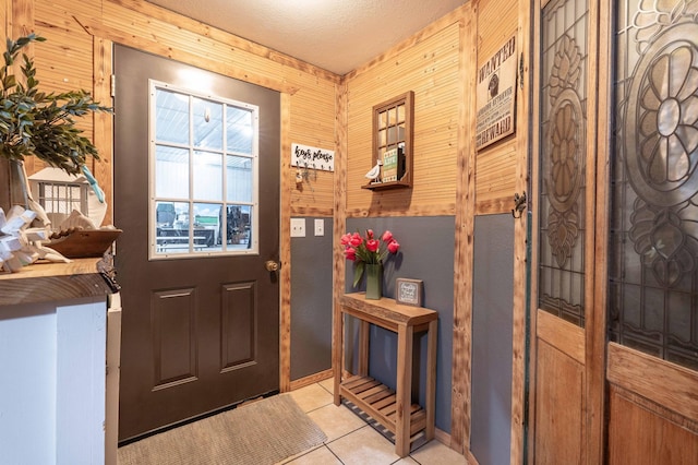 foyer entrance featuring light tile patterned floors, wooden walls, and a textured ceiling