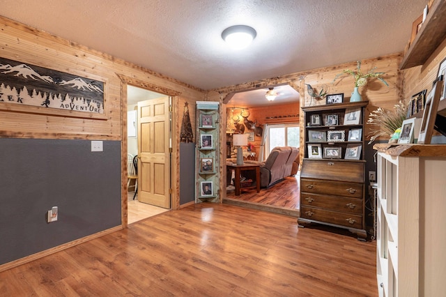 interior space with wood finished floors, arched walkways, wood walls, and a textured ceiling