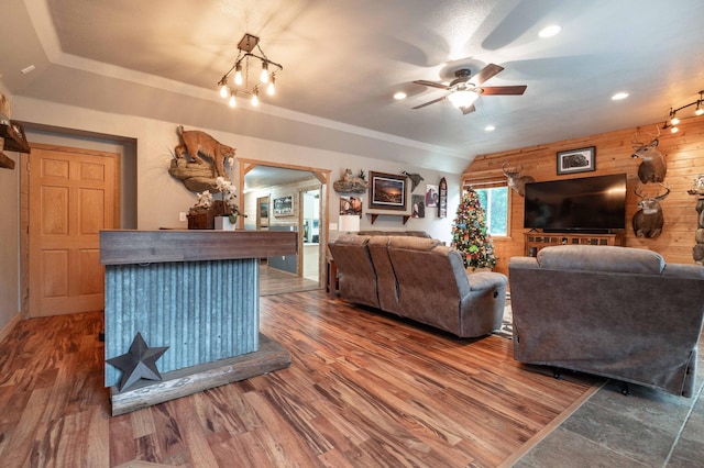 living room with lofted ceiling, wooden walls, wood finished floors, and ceiling fan