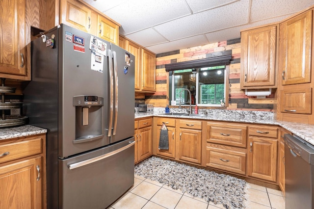 kitchen featuring a drop ceiling, light stone counters, appliances with stainless steel finishes, light tile patterned flooring, and a sink