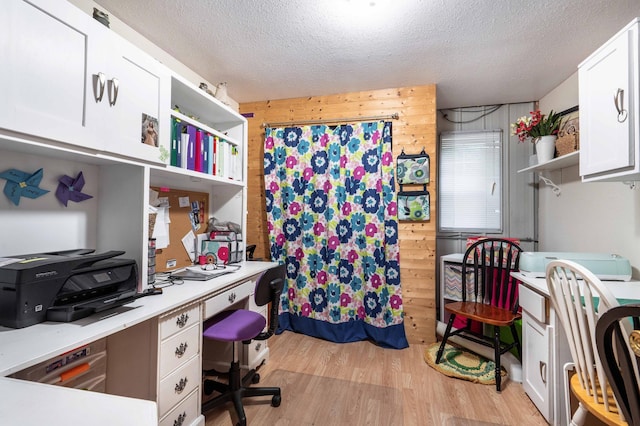 home office with light wood-style flooring, wood walls, and a textured ceiling