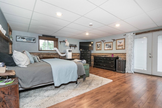 bedroom with a drop ceiling, wood finished floors, and french doors