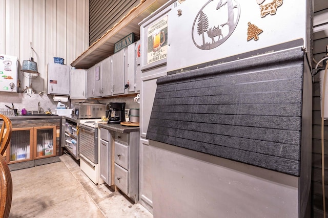 kitchen with dark countertops, a toaster, concrete flooring, electric stove, and a sink