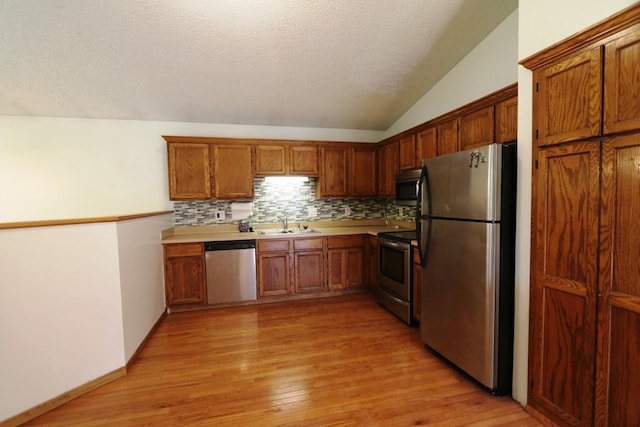 kitchen featuring vaulted ceiling, tasteful backsplash, stainless steel appliances, sink, and light wood-type flooring