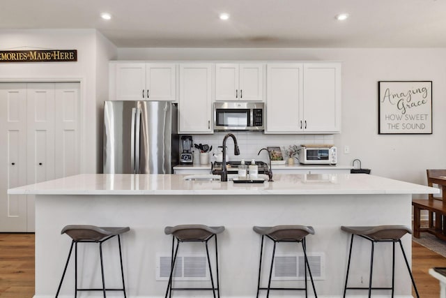 kitchen featuring stainless steel appliances, a center island with sink, white cabinets, and a kitchen bar